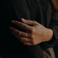Mains ornées de bagues minimalistes et d'anneaux de phalange dorés sur fond sombre.