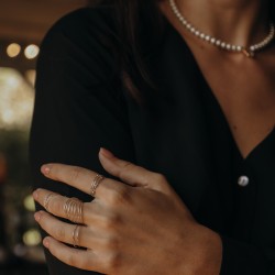Zoom sur un jeu de bagues épurées en argent 925 porté avec une robe noire et un collier de perles.