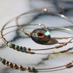 Zoom sur le sertissage du grenat bordeaux au centre de la pierre de labradorite et l'enroulement de fil d'or artisanal.