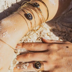 Focus sur les poignets d'une femme portant le set de joncs Una sur une peau dorée par le soleil et parsemée de sable.