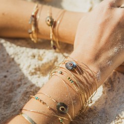 Gros plan sur la peau d'une femme à la plage portant le jonc Una en labradorite et grenat serti de la collection capsule.
