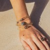Vue rapprochée du bras d'une femme allongée sur le sable, portant le set de bracelets fins Enya aux reflets dorés et minéraux.